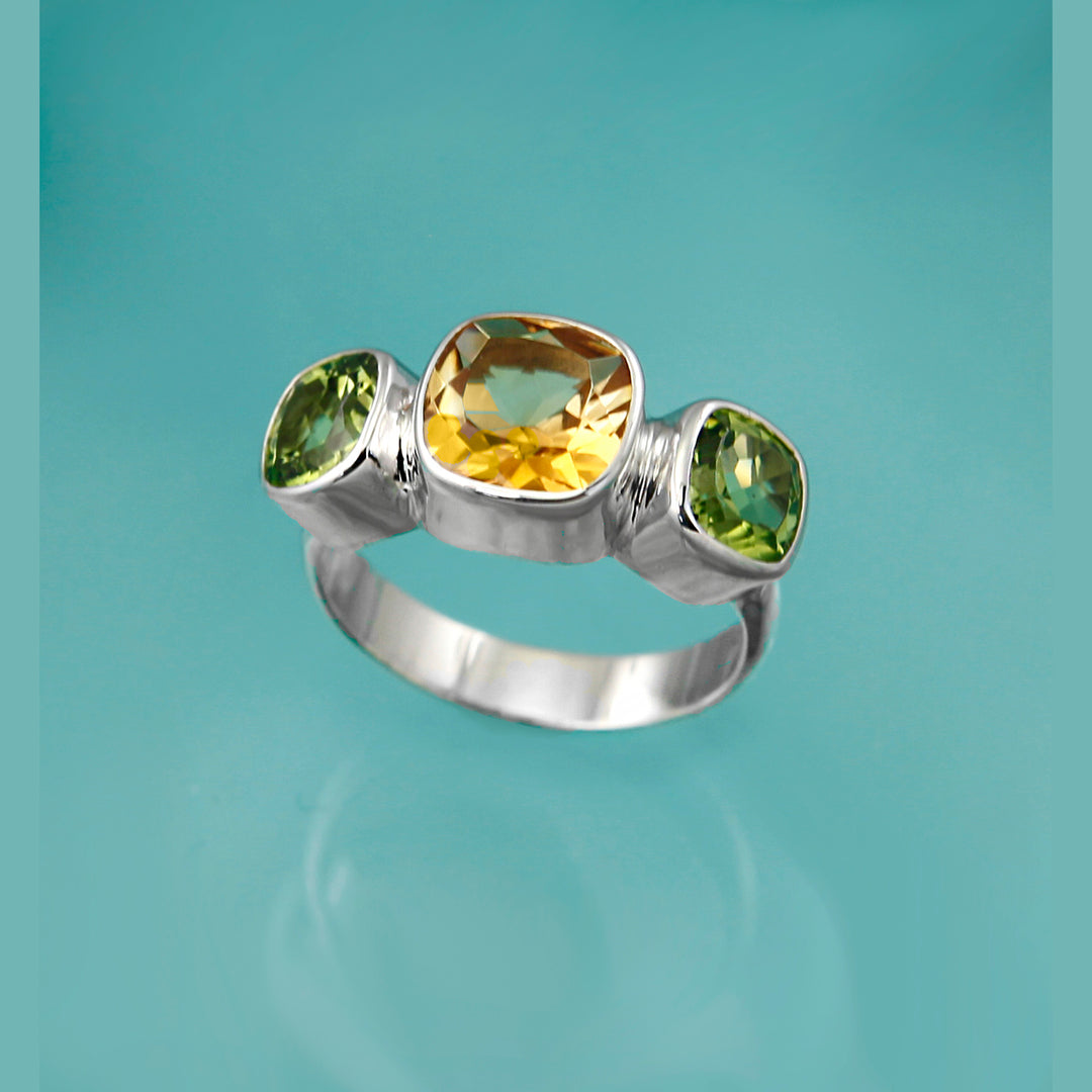 Cushion-cut citrine and peridot gemstones set in a silver ring on a turquoise background