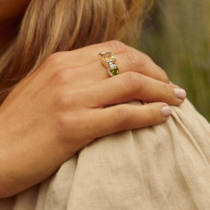 Model wearing a green and yellow gemstone ring in a garden