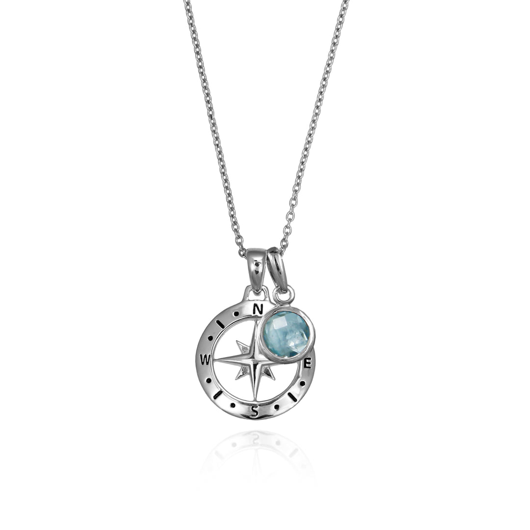 Silver compass necklace with a blue topaz march december birthstone charm pendant and chain on a white background