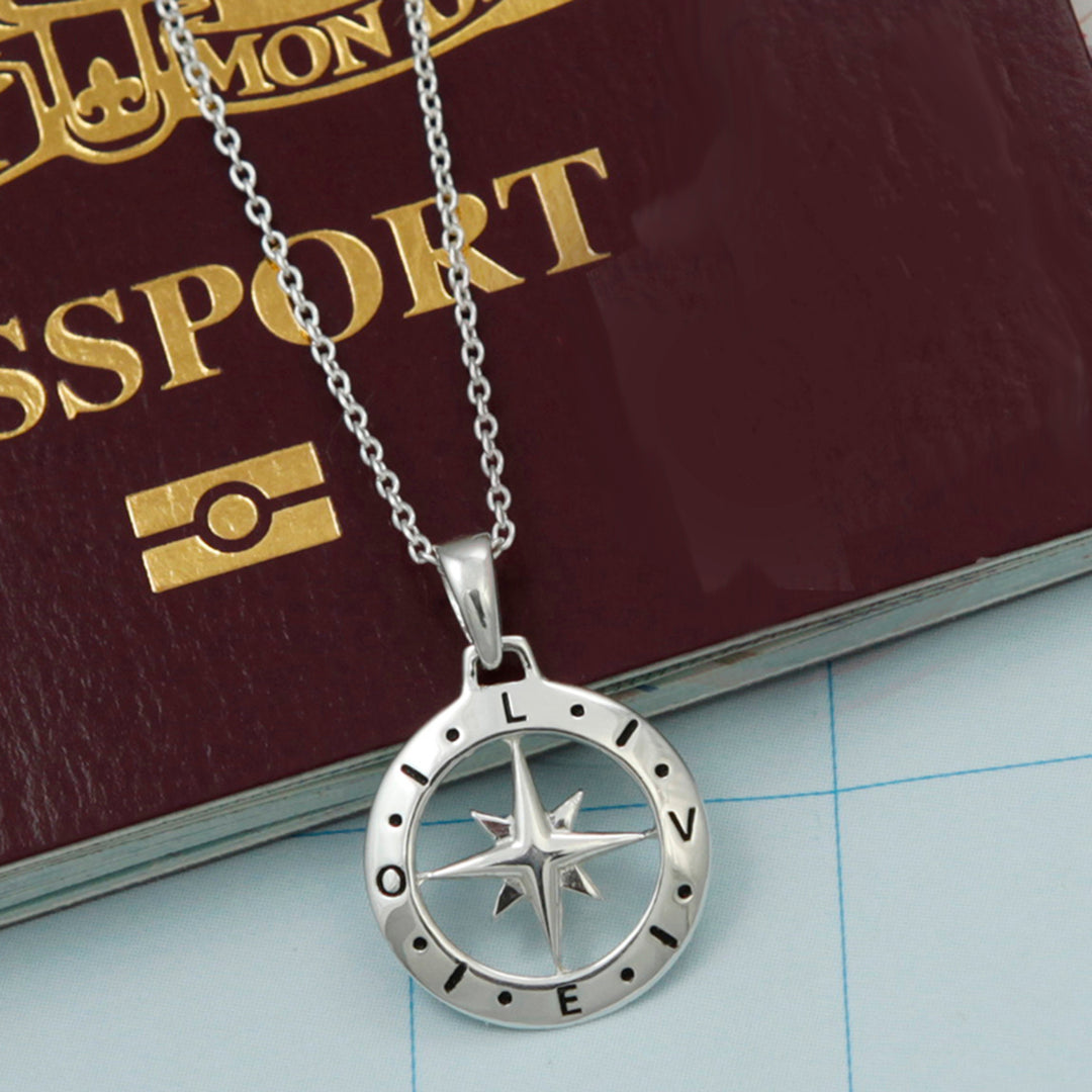 Sterling silver compass pendant necklace with the word love engraved on it on top of a passport