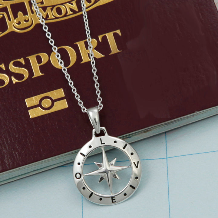 Sterling silver compass pendant necklace with the word love engraved on it on top of a passport