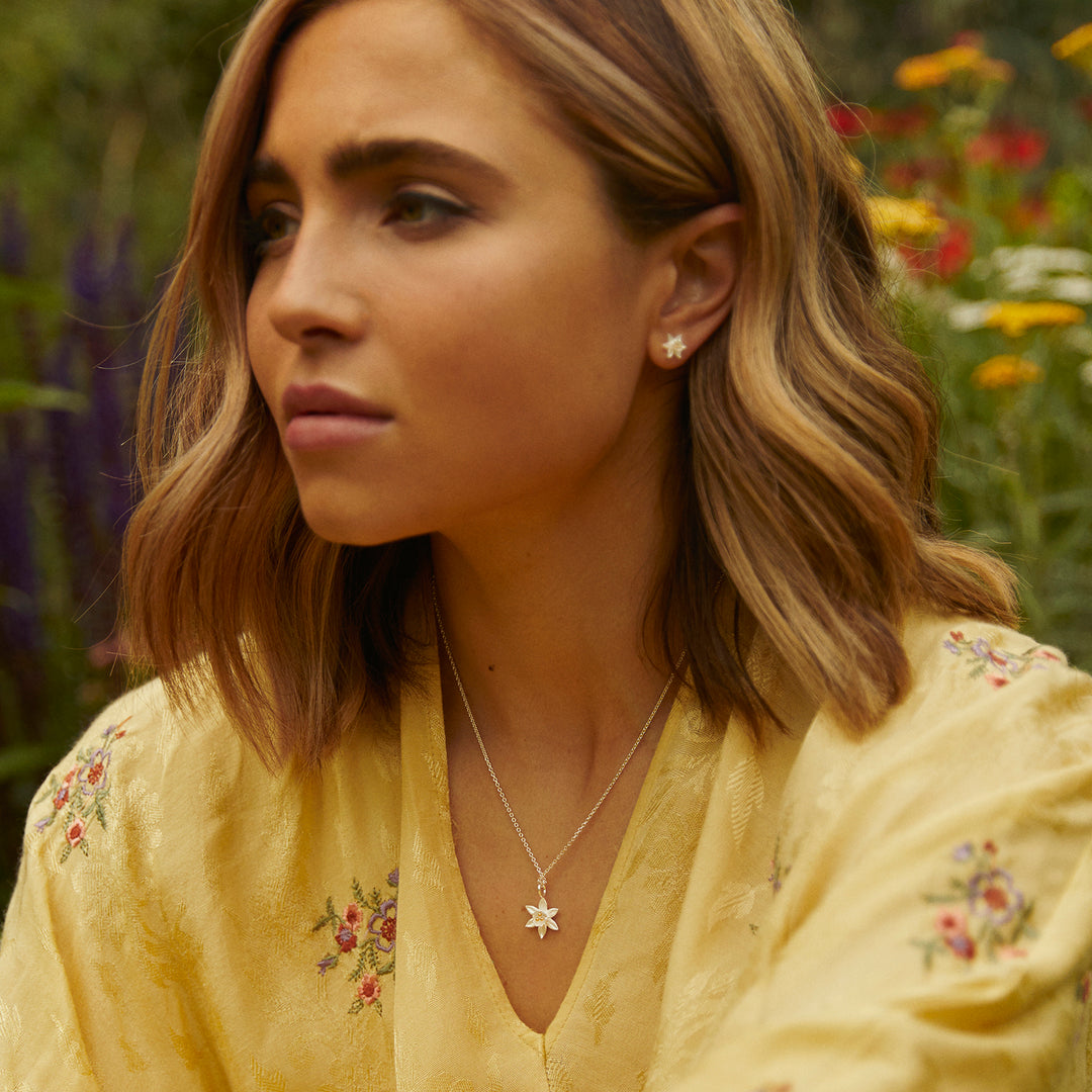 Woman wearing silver daffodil stud earrings and necklace against a natural background