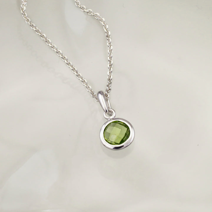 Silver necklace with a green gemstone pendant on a light gray background