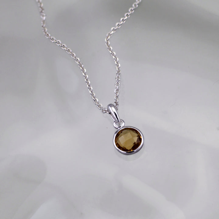smoky quartz birthstone pendant set in sterling silver on a gray background