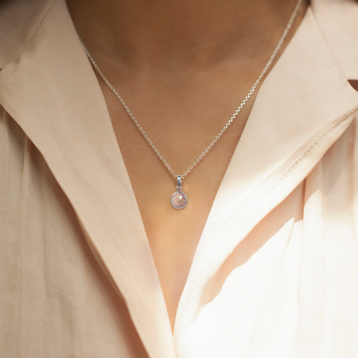 Close-up of model wearing a pretty silver pendant with a white topaz faceted gem
