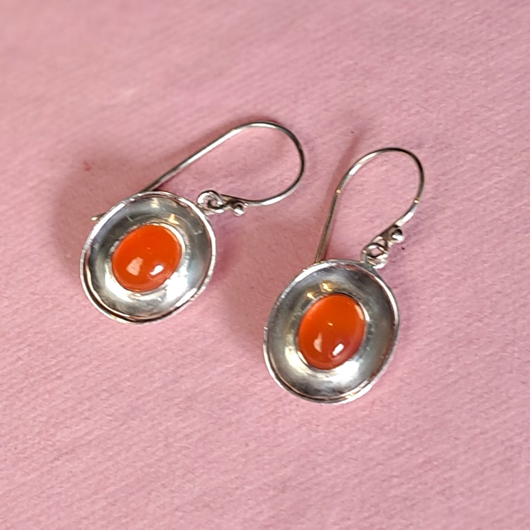 Alternative view of sterling silver dish shaped drop earrings with carnelian on a pink background