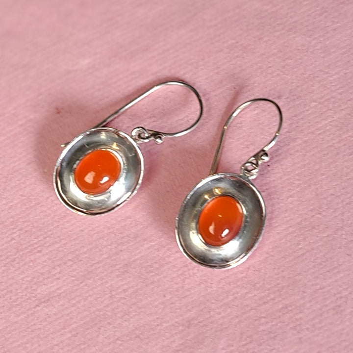 Alternative view of sterling silver dish shaped drop earrings with carnelian on a pink background