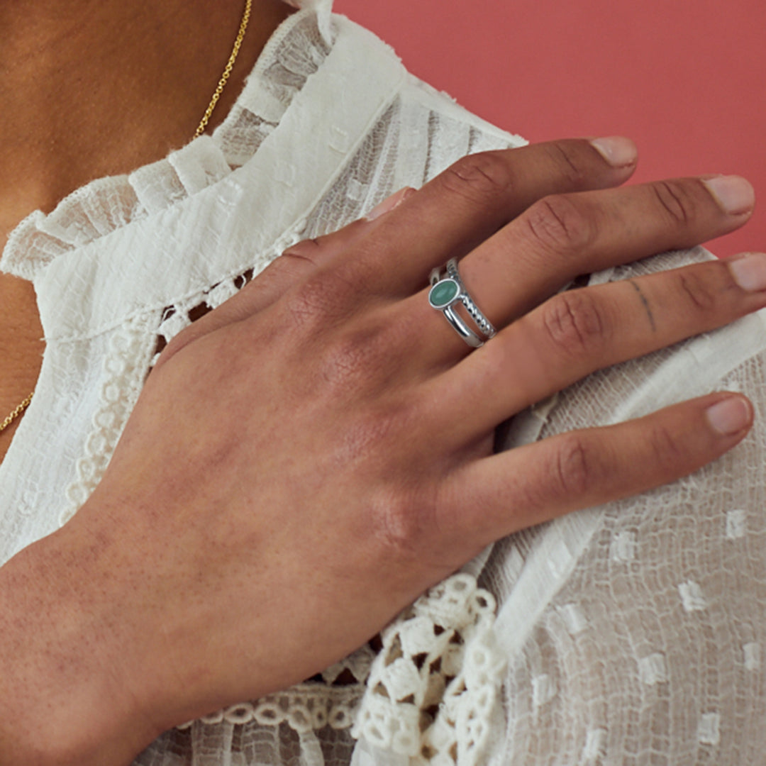 Model wearing a silver and green stone ring on a pink background