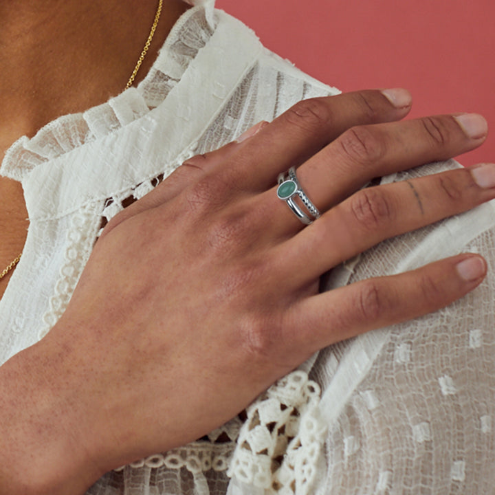 Model wearing a silver and green stone ring on a pink background