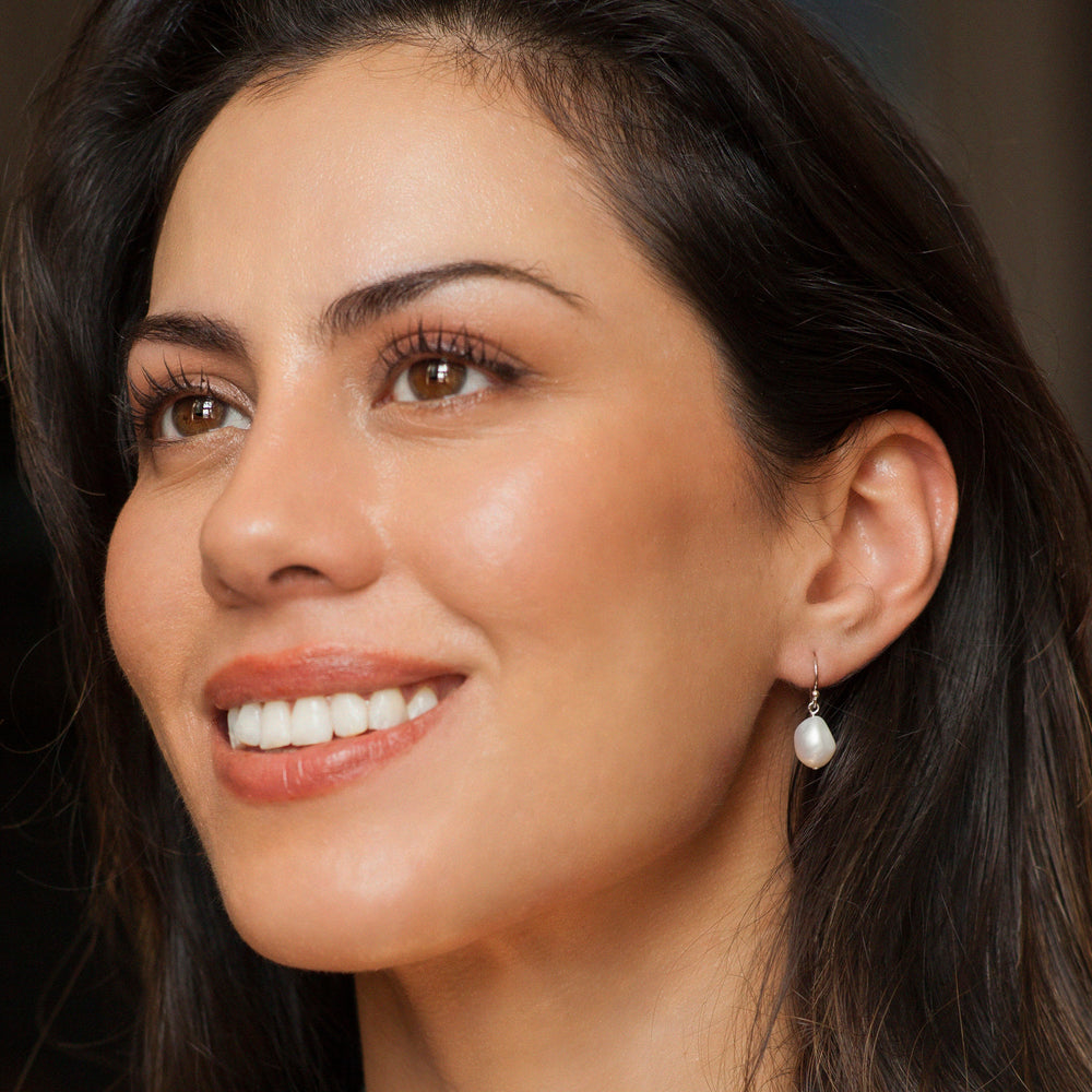 Close-up of a woman wearing pearl earrings with a neutral background