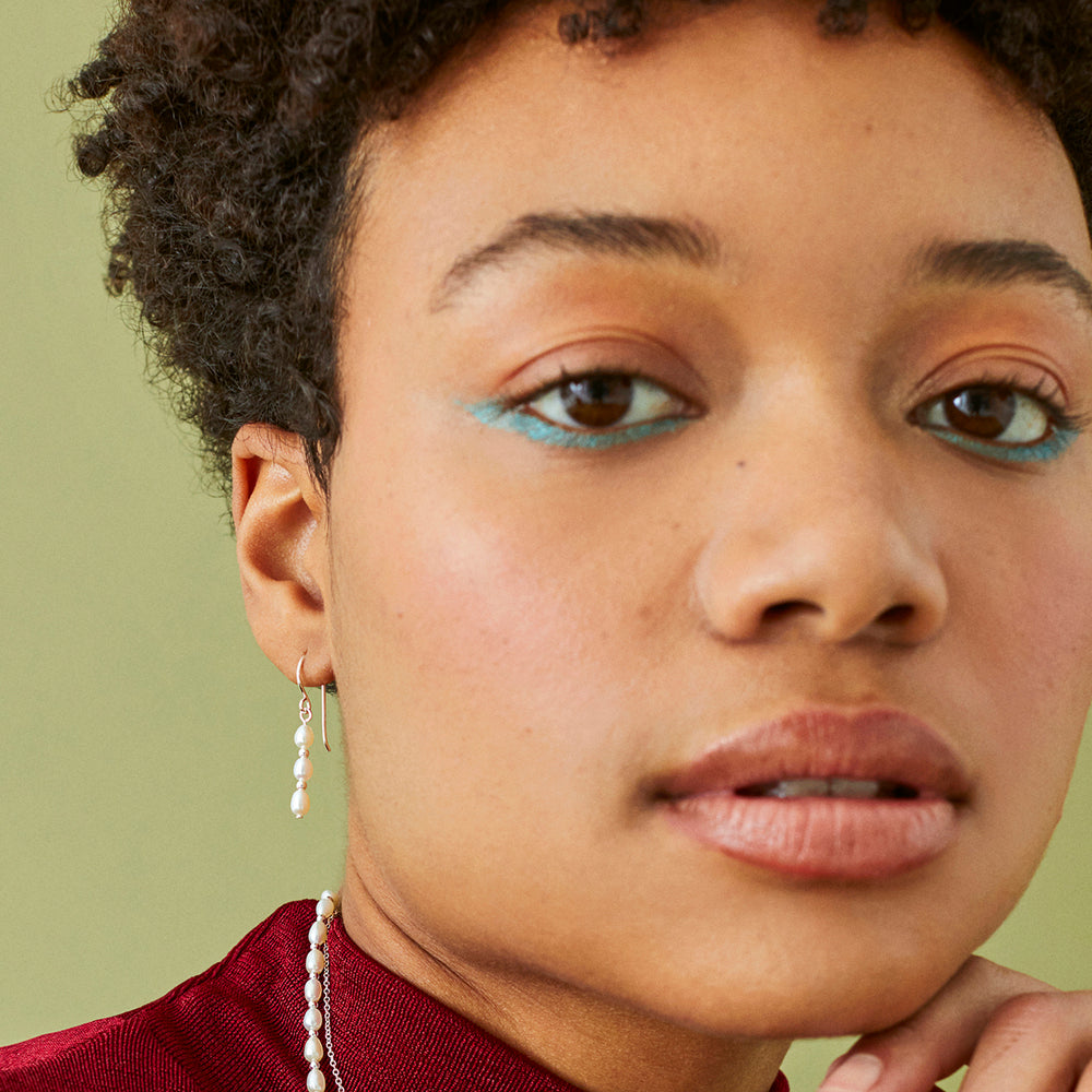 Close-up of a model wearing dainty triple pearl earrings in silver