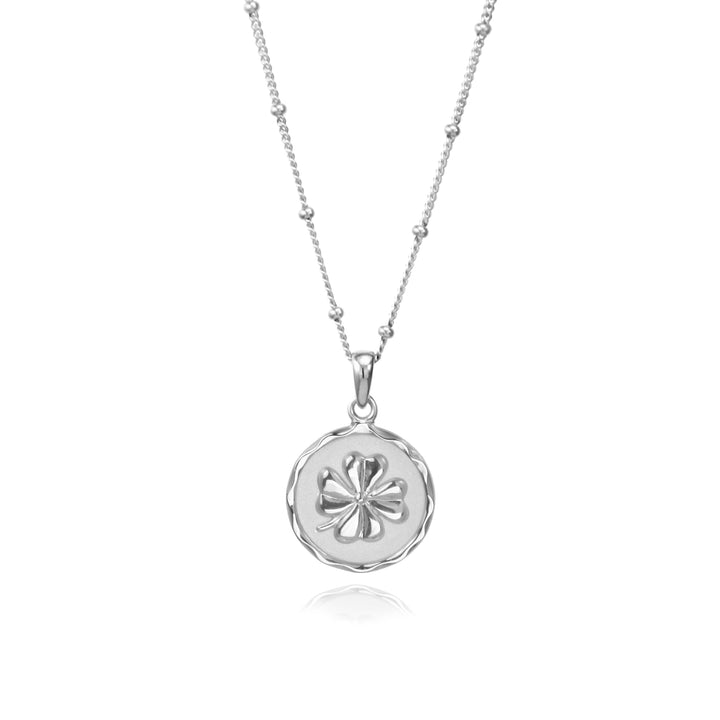 Silver four-leaf clover necklace on a beaded chain against a white background