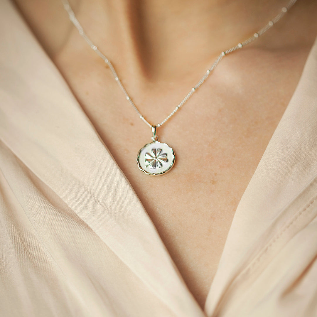 Close-up of model wearing a silver four-leaf clover pendant and a cream blouse.