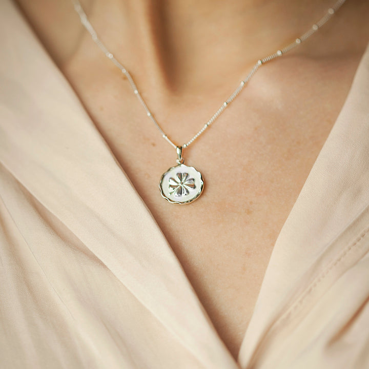 Close-up of model wearing a silver four-leaf clover pendant and a cream blouse.