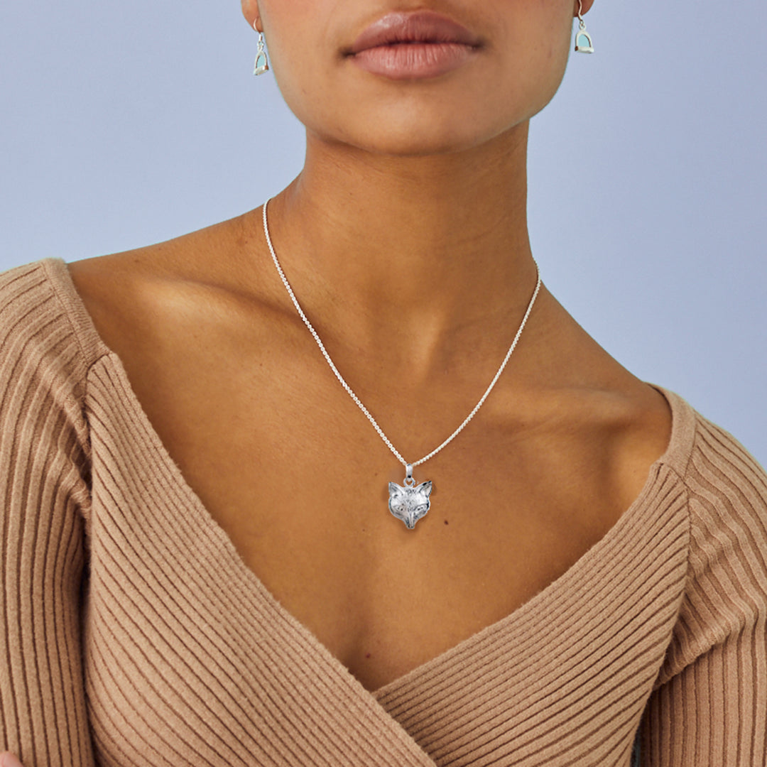Woman wearing a silver necklace with a fox head pendant against a light blue background