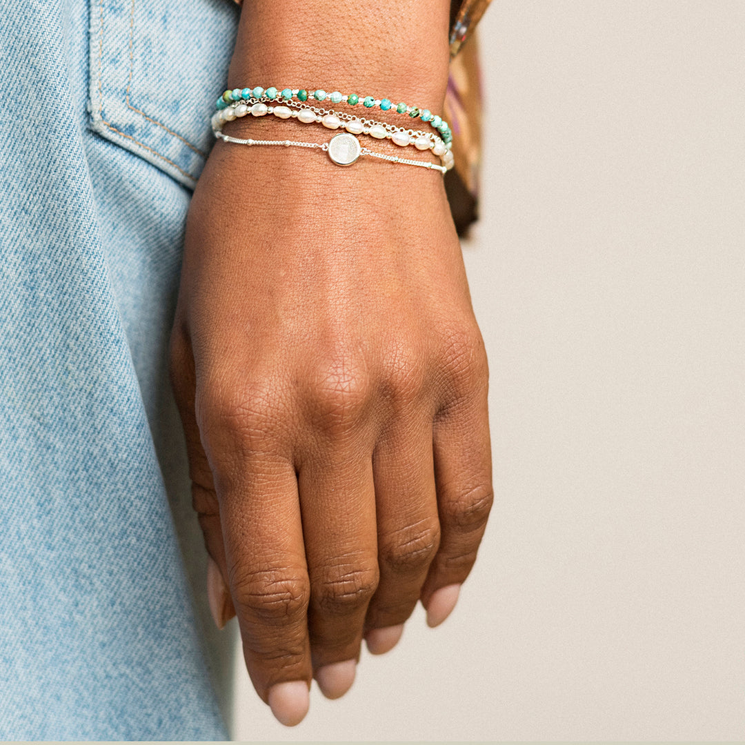 Hand wearing multiple bracelets in silver with moonstone and white pearl