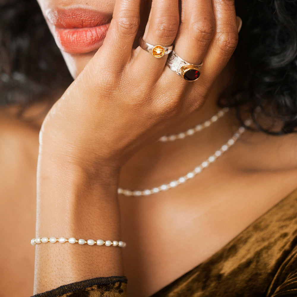 Close-up of a hand wearing two rings with gemstones and a silver pearl bracelet.