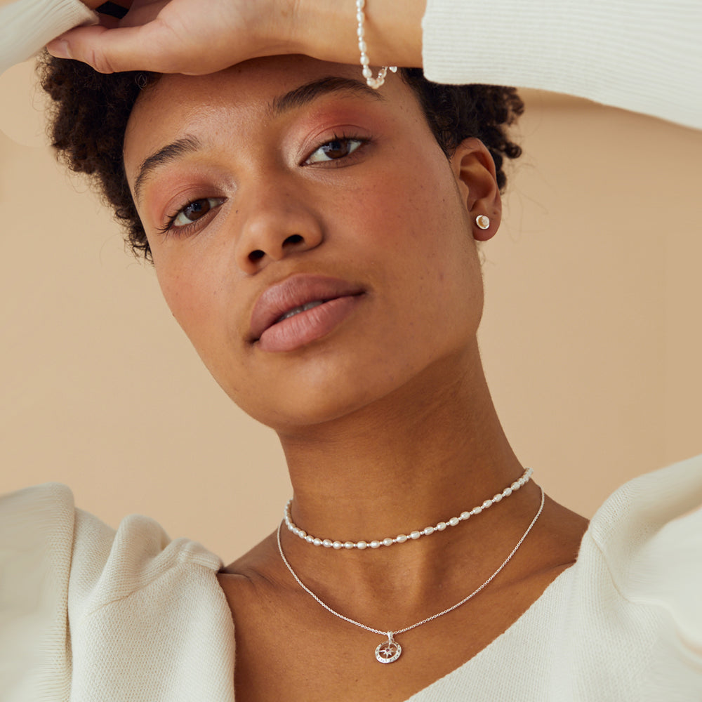 Woman wearing a delicate pearl choker and compass birthstone necklace with pearl studs and bracelet.