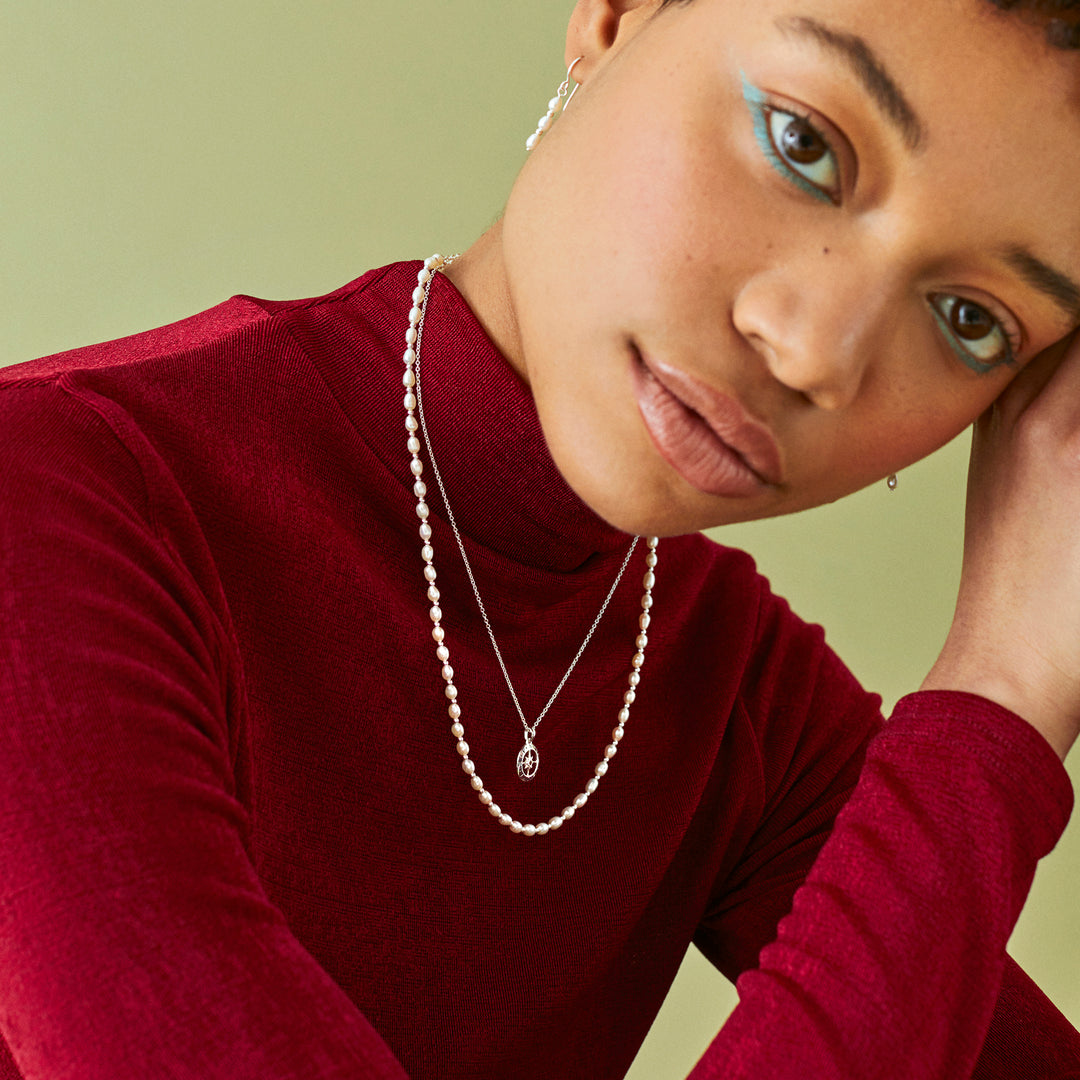 Woman wearing a red turtleneck and pearl necklace with matching earrings