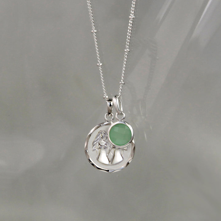 Silver gemini zodiac pendant and green quartz May birthstone charm on a gray background