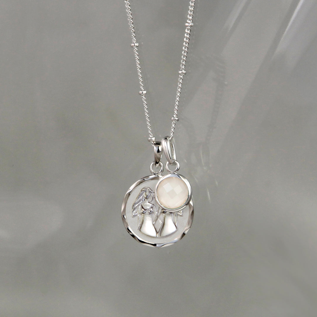 Silver gemini zodiac pendant and moonstone June birthstone charm on a gray background
