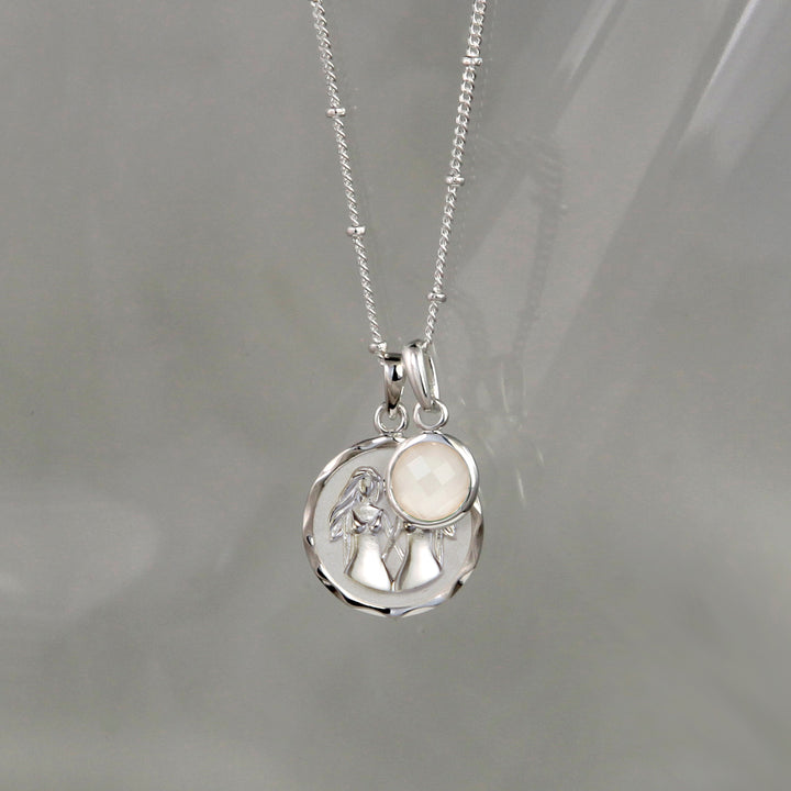 Silver gemini zodiac pendant and moonstone June birthstone charm on a gray background