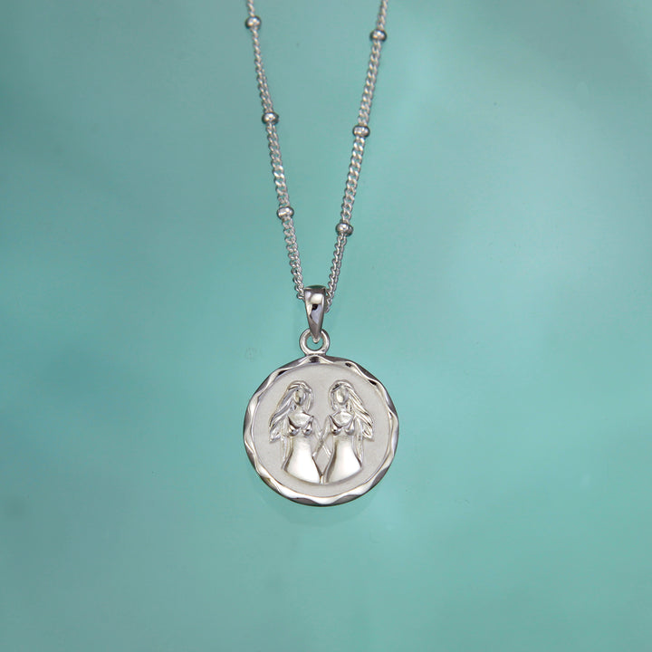 Silver gemini twins zodiac pendant on an aqua background