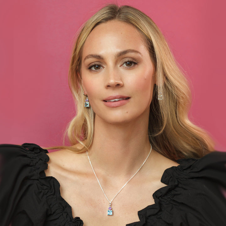 Woman wearing a silver earring and necklace set with blue topaz and amethyst gemstones