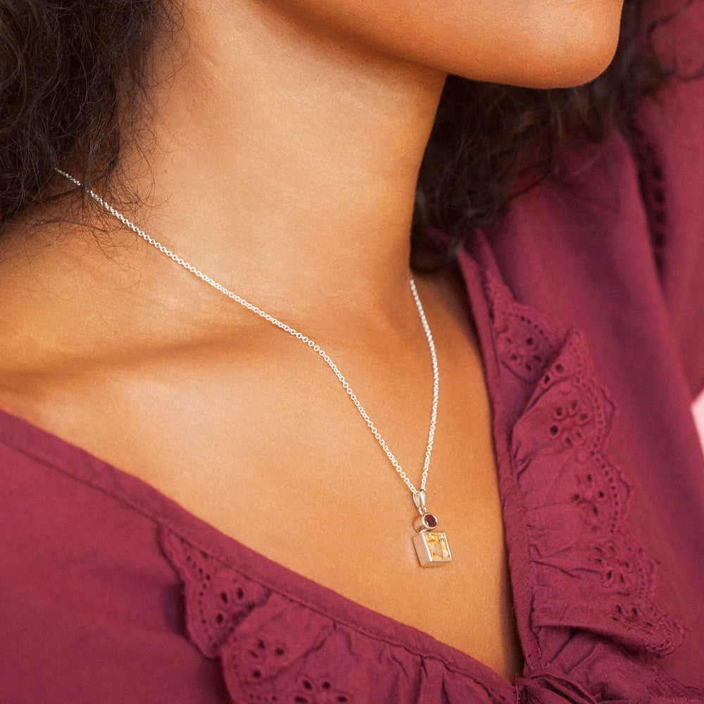 Close-up of a person wearing a silver necklace with a citrine and garnet pendant