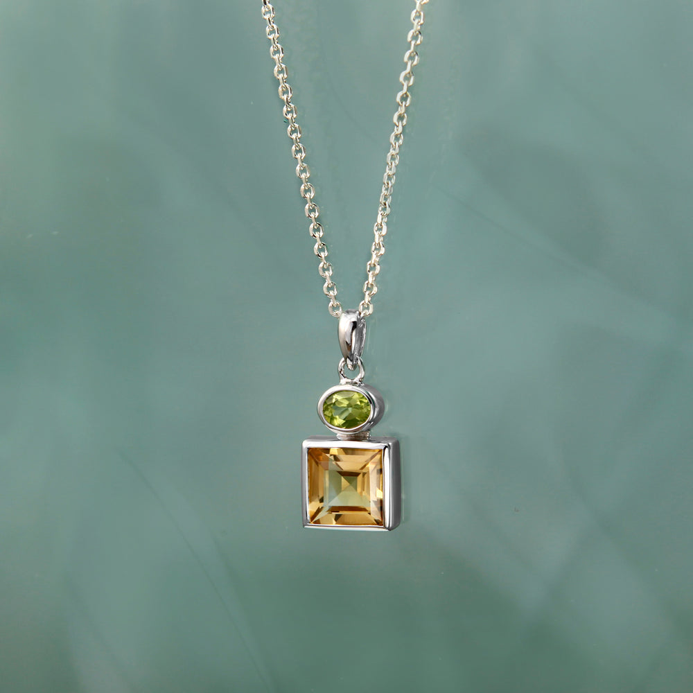 Silver necklace with a square-cut citrine and an oval peridot gemstone pendant on a green background