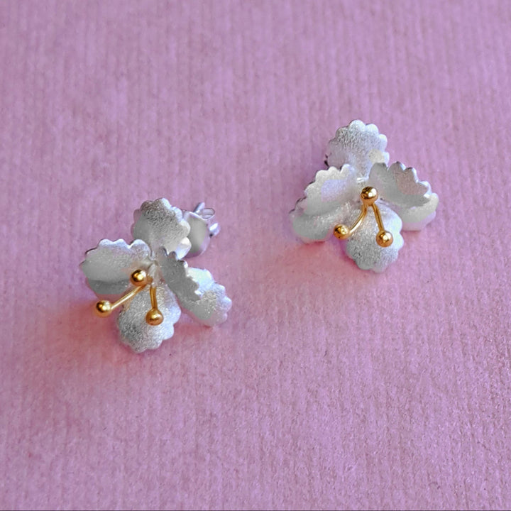 Alternative view of sterling silver and gold vermeil cherry blossom stud earrings on pink background