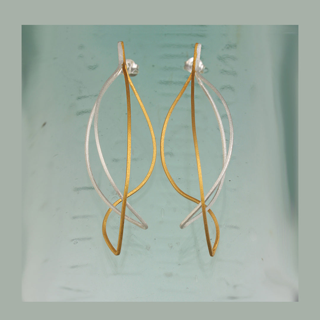 Pair of gold and silver delicate post earrings on a light green background