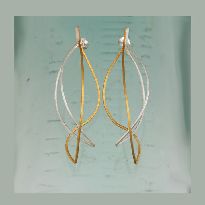 Pair of gold and silver delicate post earrings on a light green background
