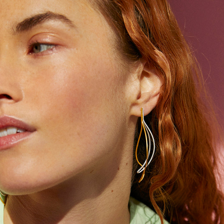 Close-up of a red haired woman wearing silver and gold statement earrings 