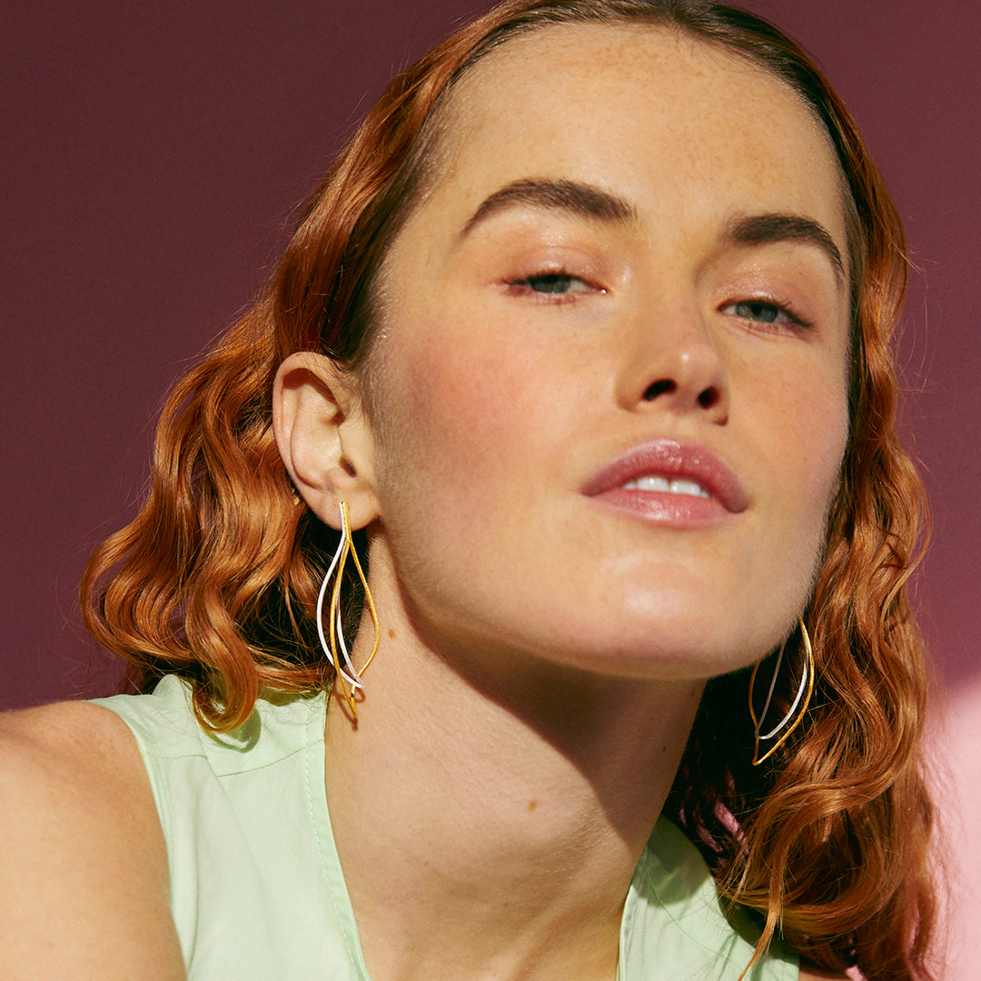 Close-up of a woman with wavy hair wearing gold and silver post earrings against a purple background