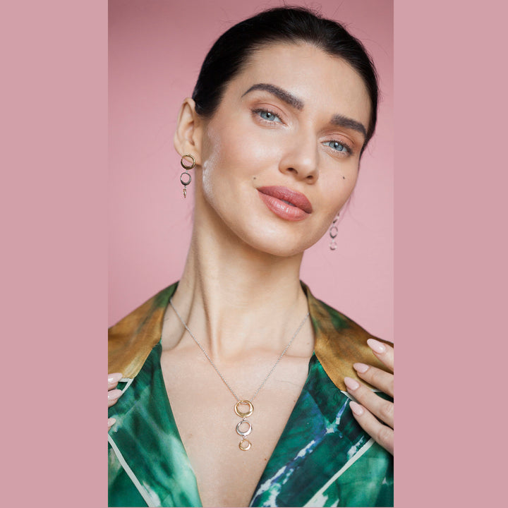 Woman wearing gold and silver necklace and earrings against a pink background