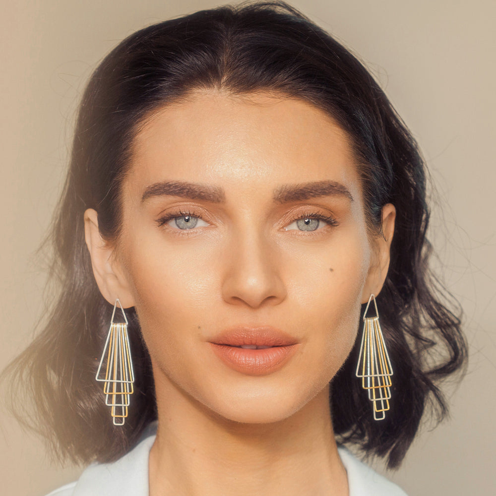 Woman wearing gold and silver geometric earrings against a neutral background