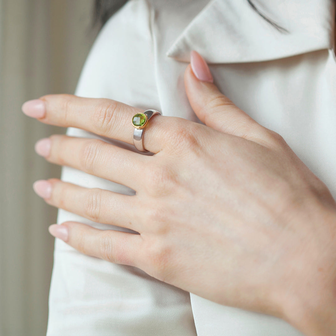 Close-up of a hand wearing a silver ring with a green gemstone on a neutral background