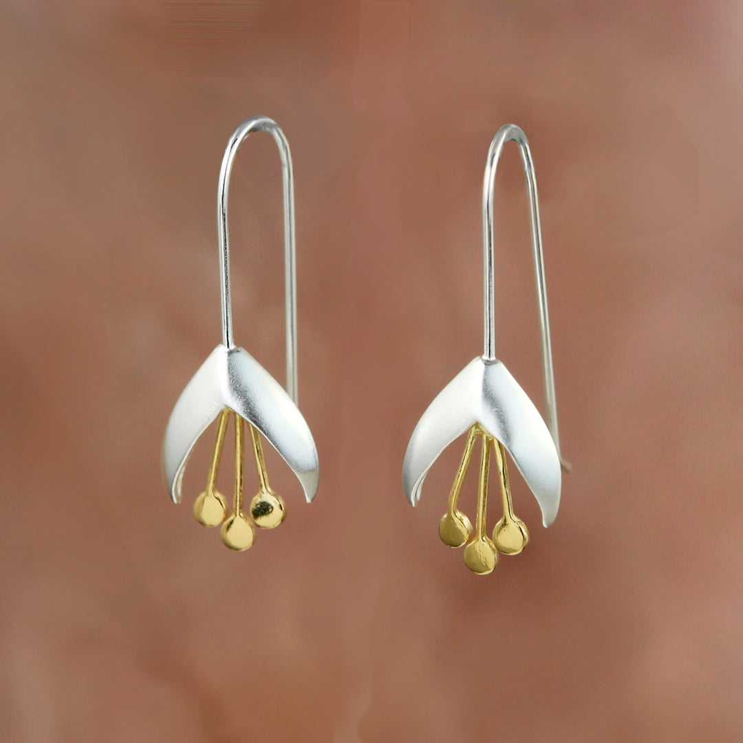 Silver snowdrop flower earrings with gold accents on a brown background