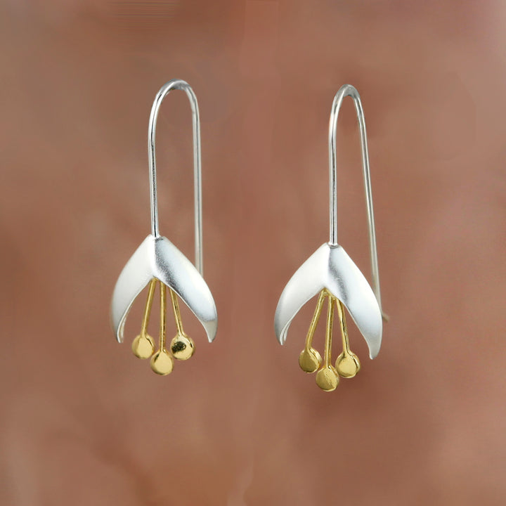 Silver snowdrop flower earrings with gold accents on a brown background
