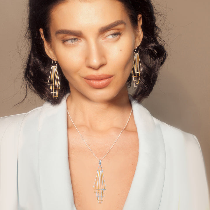 Woman wearing silver and gold earrings and matching necklace against a neutral background