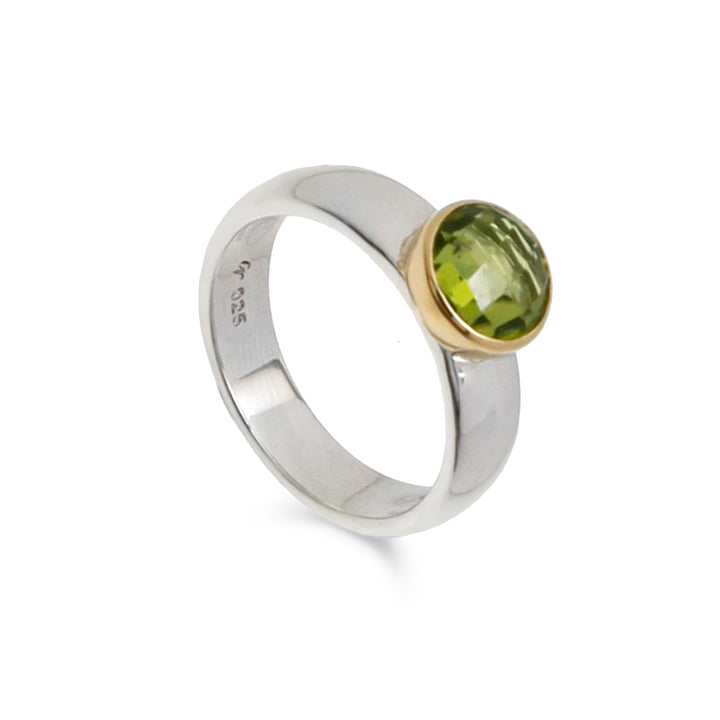 Silver band ring with a round peridot gemstone set in a gold bezel against a white background
