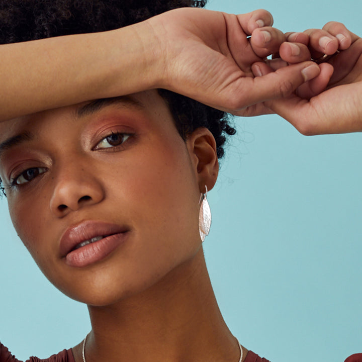 Woman wearing shiny hammered silver earrings on a blue background