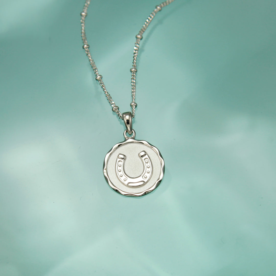 Silver necklace with a round pendant featuring a horseshoe design on a light green background.