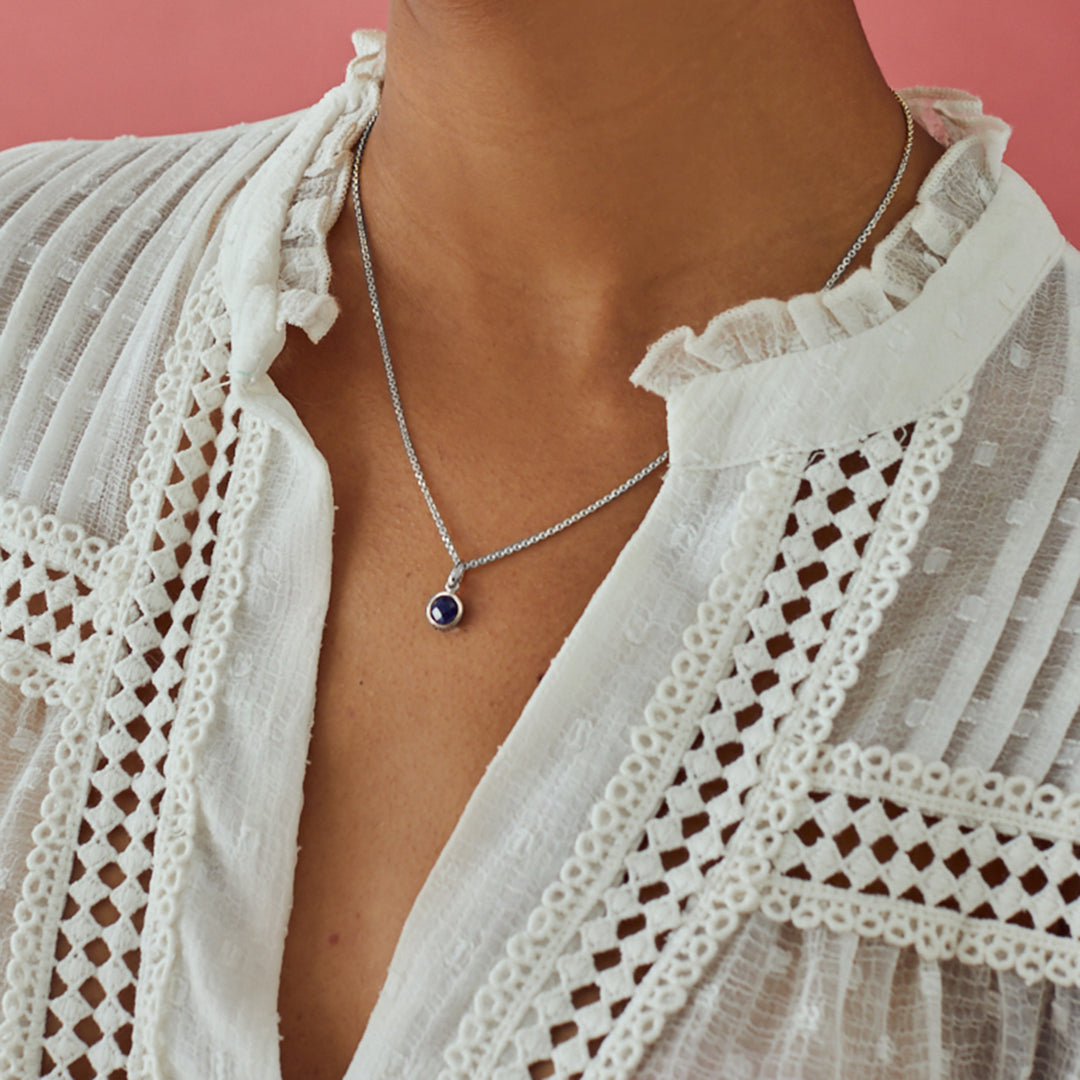 Close-up of model wearing a dainty silver pendant with a round dark blue lapis lazuli stone.