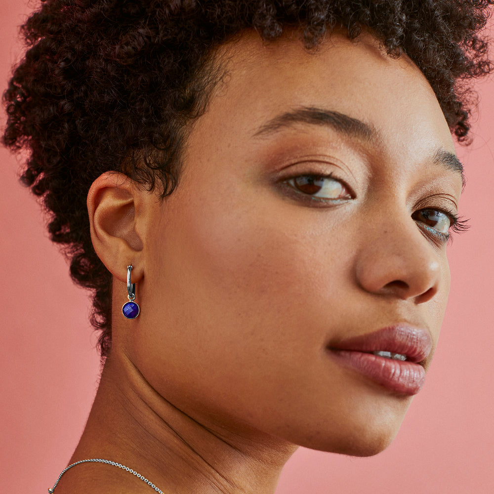 Close-up of model wearing silver huggie hoop earrings with genuine lapis lazuli stones.