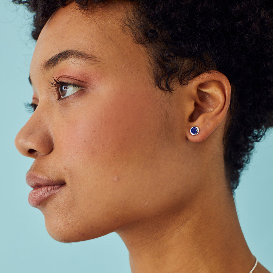 Close-up of a woman wearing dark blue gemstone stud earring against a light blue background