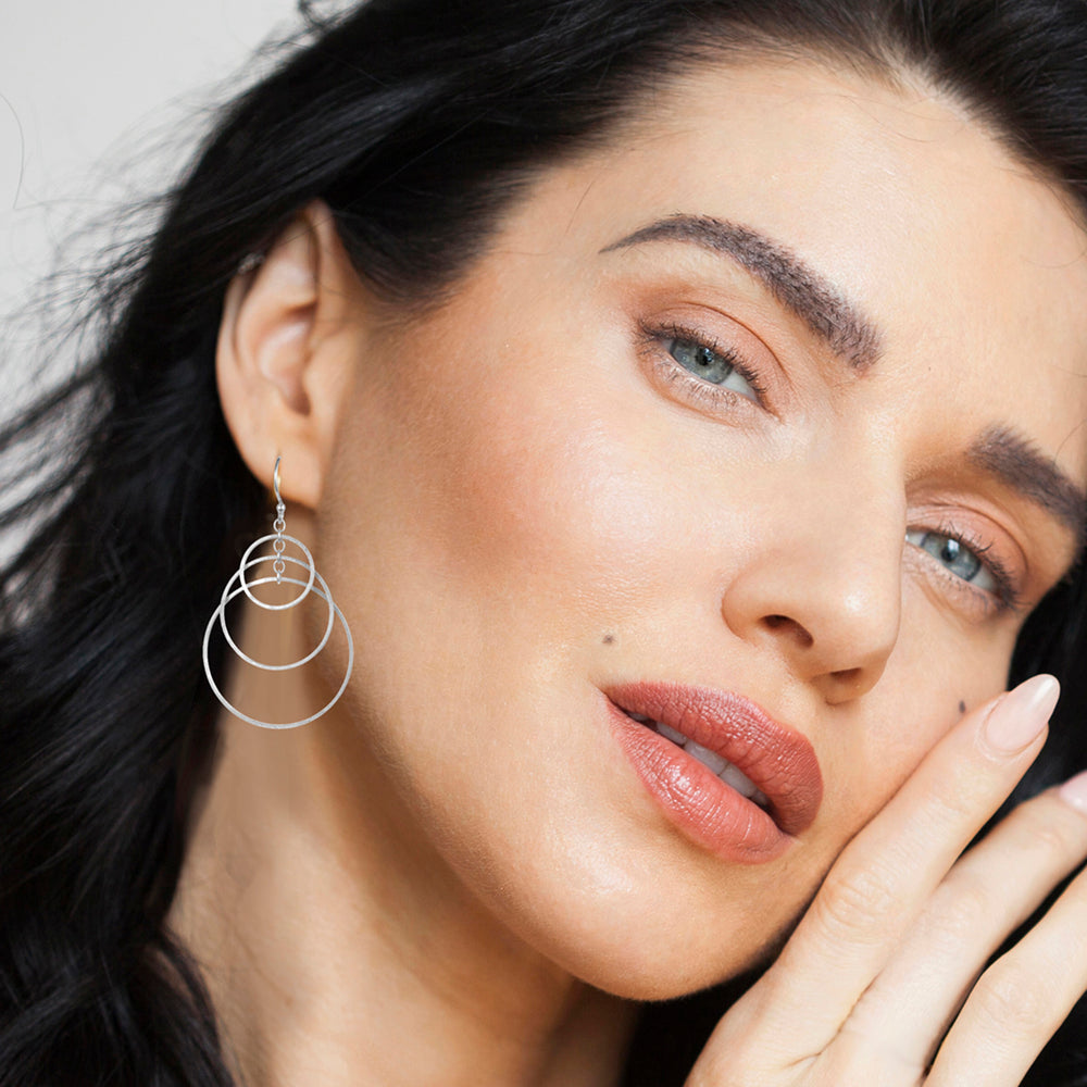 Close-up of a woman wearing silver hoop earrings with a neutral background