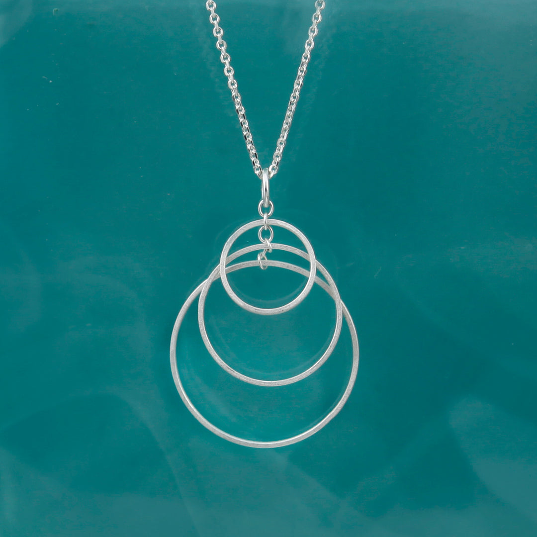 Silver necklace with three interlocking rings on a teal background