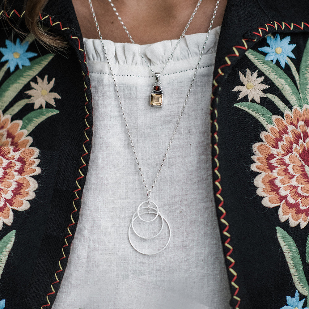 Close-up of model wearing silver three hoop necklace and a embroidered jacket